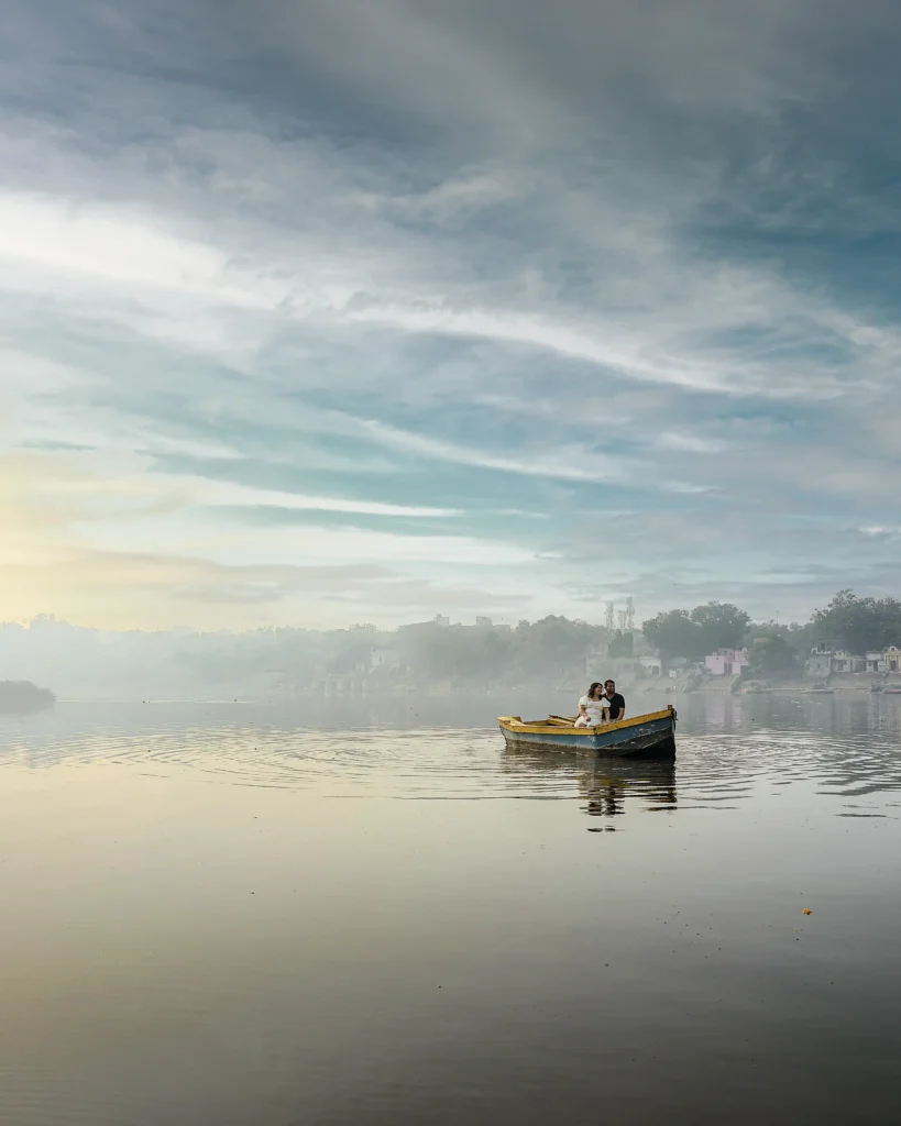 Wide cinematic pre wedding shoot at Yamuna Ghat during sunrise with soft river light and natural atmosphere