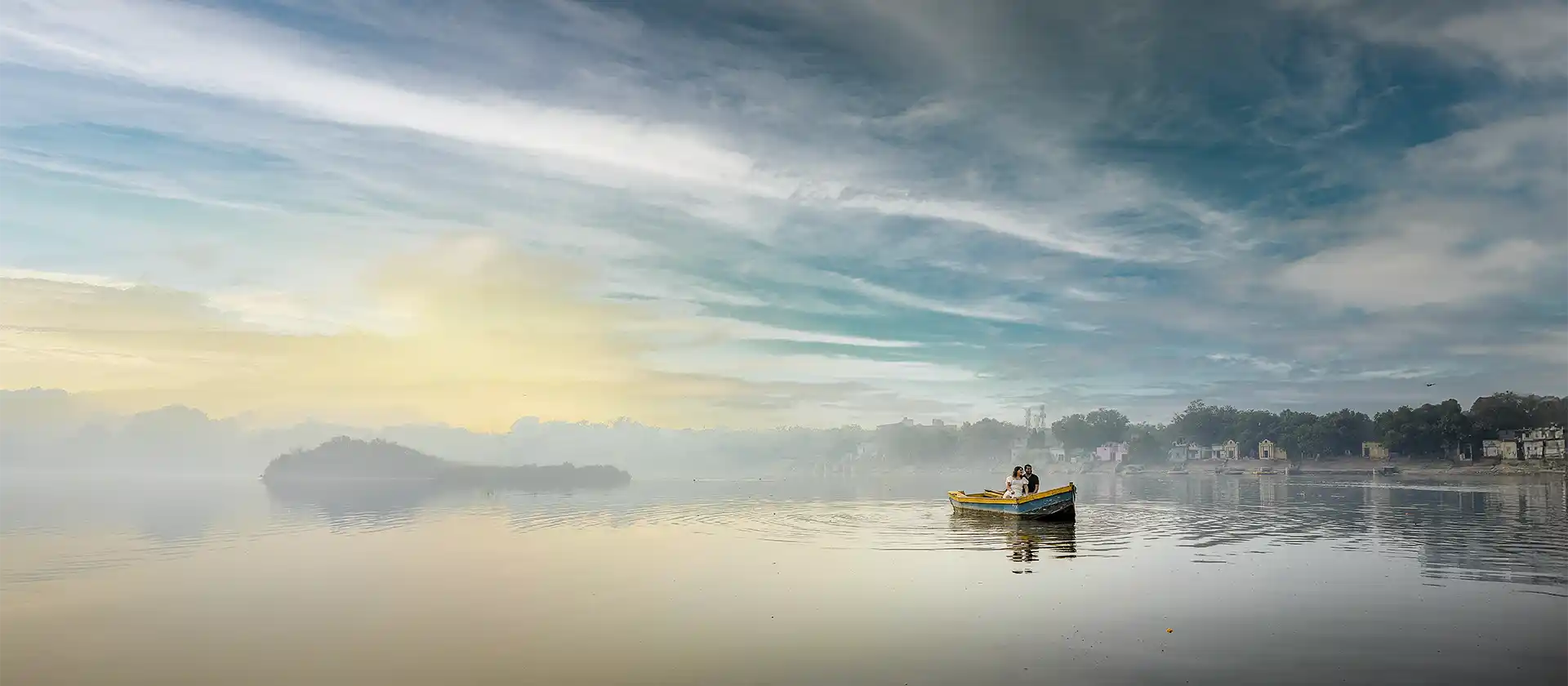 Couple during a pre-wedding photography session on a small boat at sunrise across a tranquil lake.
