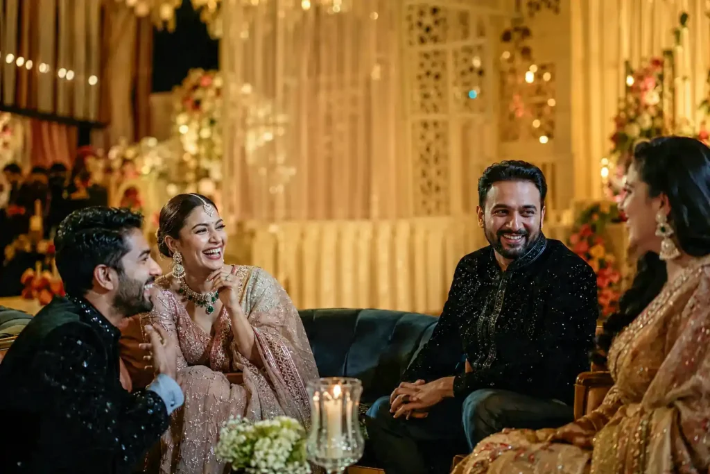 Wedding guests sharing a joyful candid moment while the bride and groom experience a different moment in the background during an Indian wedding celebration